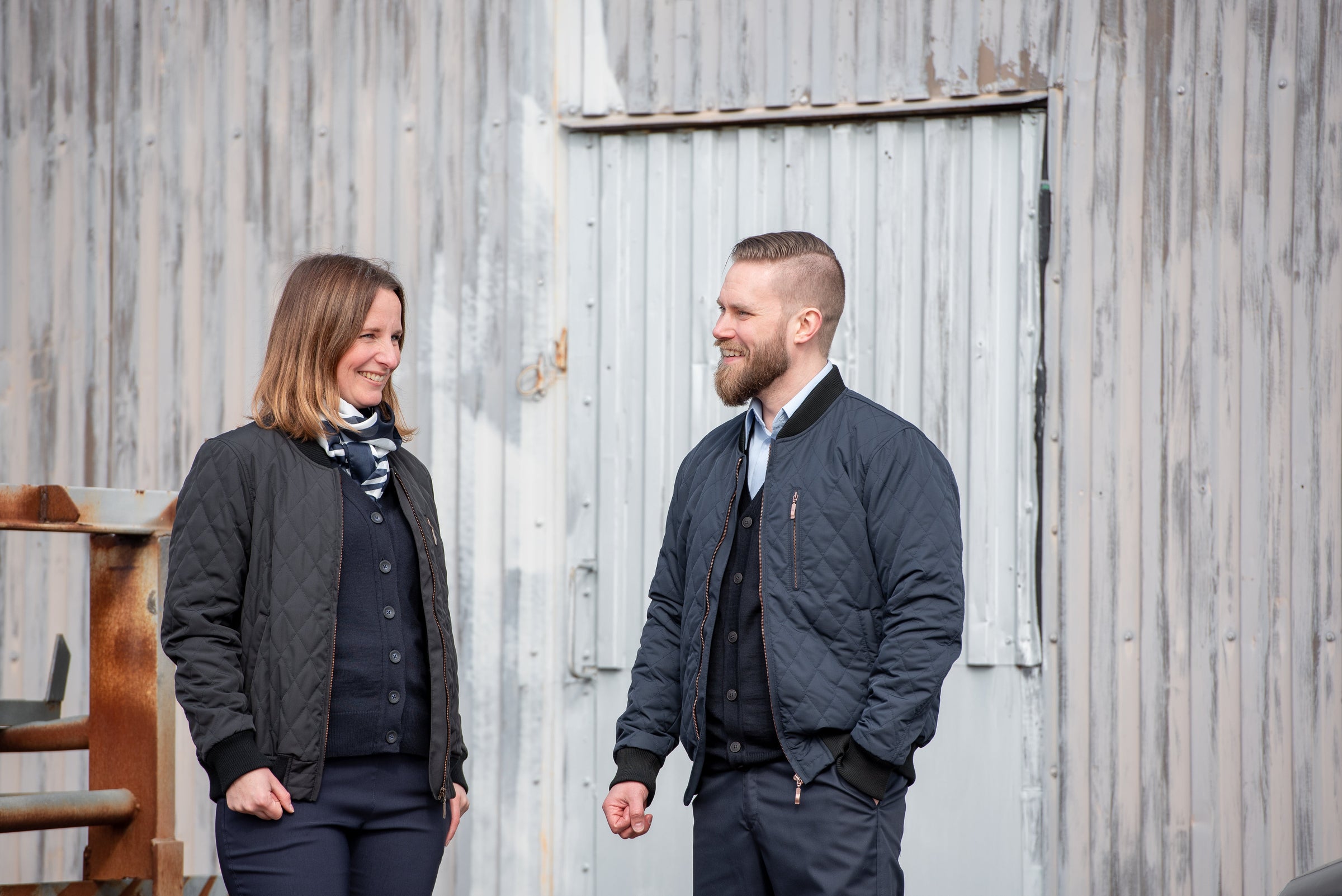 Nais-ja mieskuljettajalla päällä kuvassa Image Wearin mallistosta musta ja tummansininen tikkitakki sekä takin alla neuletakki, kauluspaita ja suorat housut.