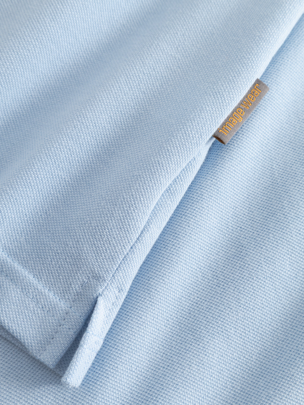 Yksityiskohtakuva vaaleansinisen naisten pikeepaidan sivusauman pikkuhalkiosta ja Image Wearin tuotemerkistä.