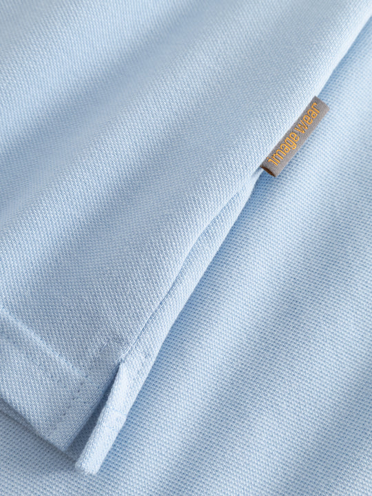 Yksityiskohtakuva vaaleansinisen naisten pikeepaidan sivusauman pikkuhalkiosta ja Image Wearin tuotemerkistä.