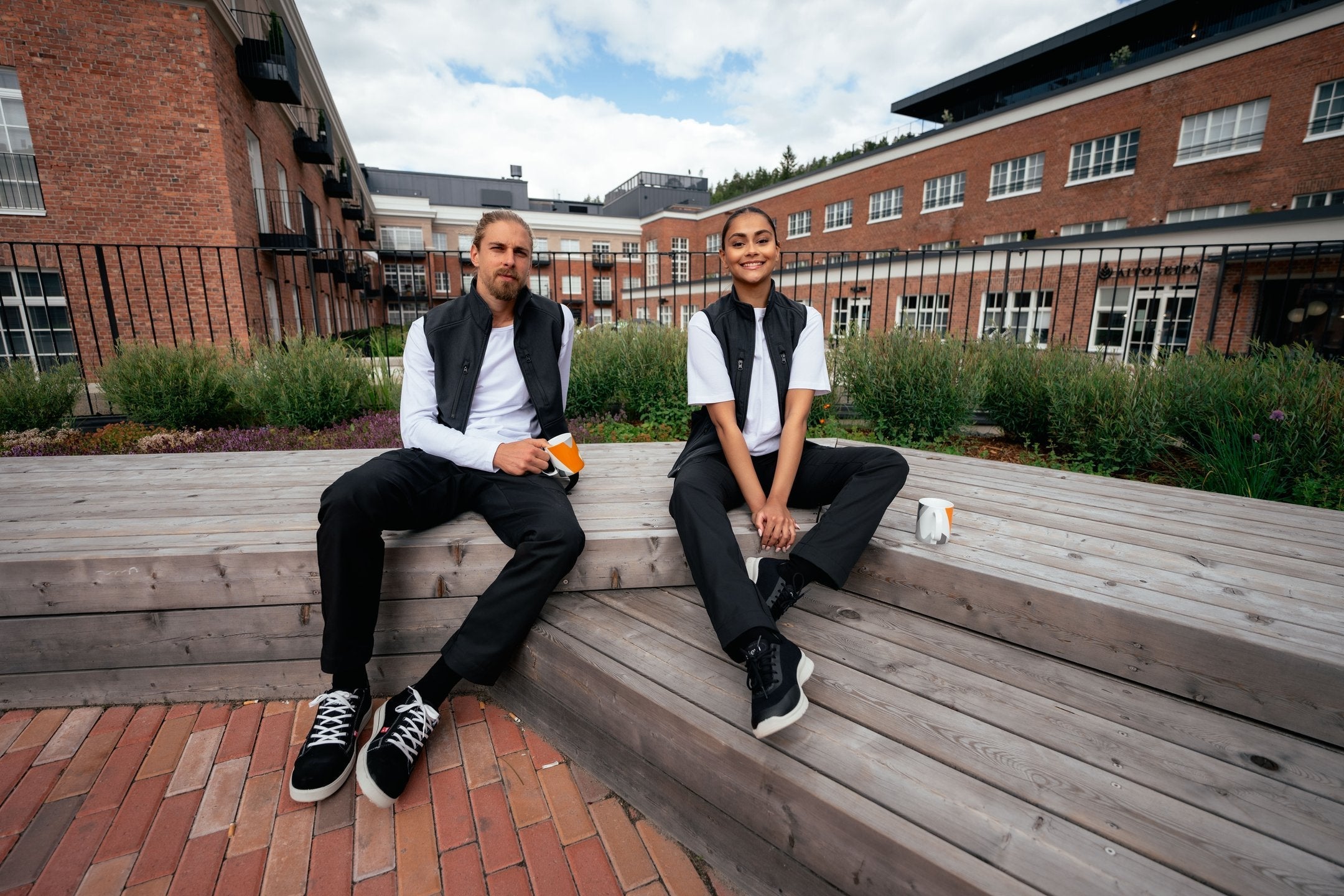 Kuvassa nainen ja mies kävelevät ulkona. Molemmilla on päällä softshell takit Image Wearin valikoimasta ja mustat joustavat työfarkut sekä Sievin työkengät. 