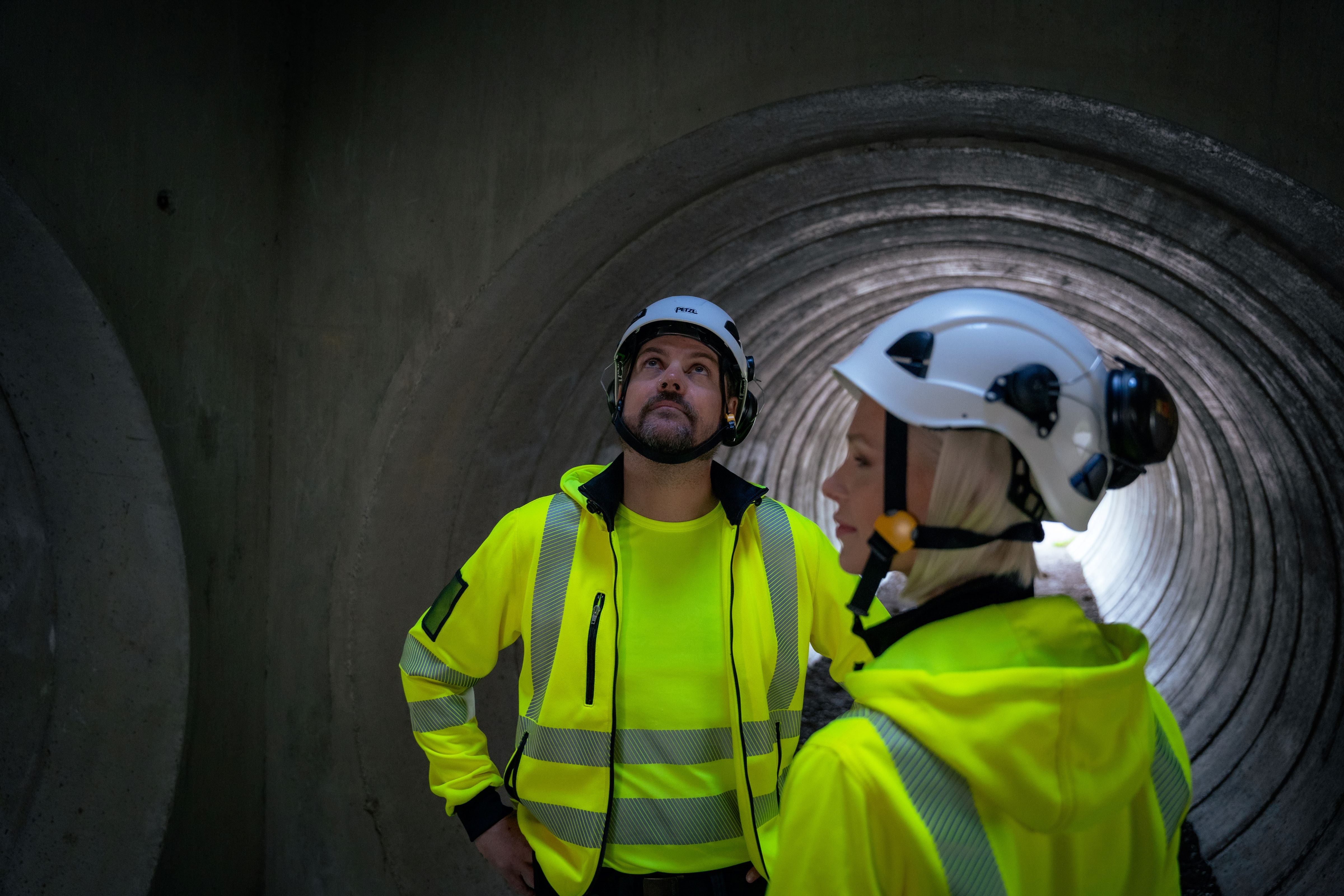 Kuvassa mies ja nainen tunnelissa. Kummallakin on päällään valkoinen kypärä ja Image Wearin huomioväriset keltaiset hupparit ja t-paidat.