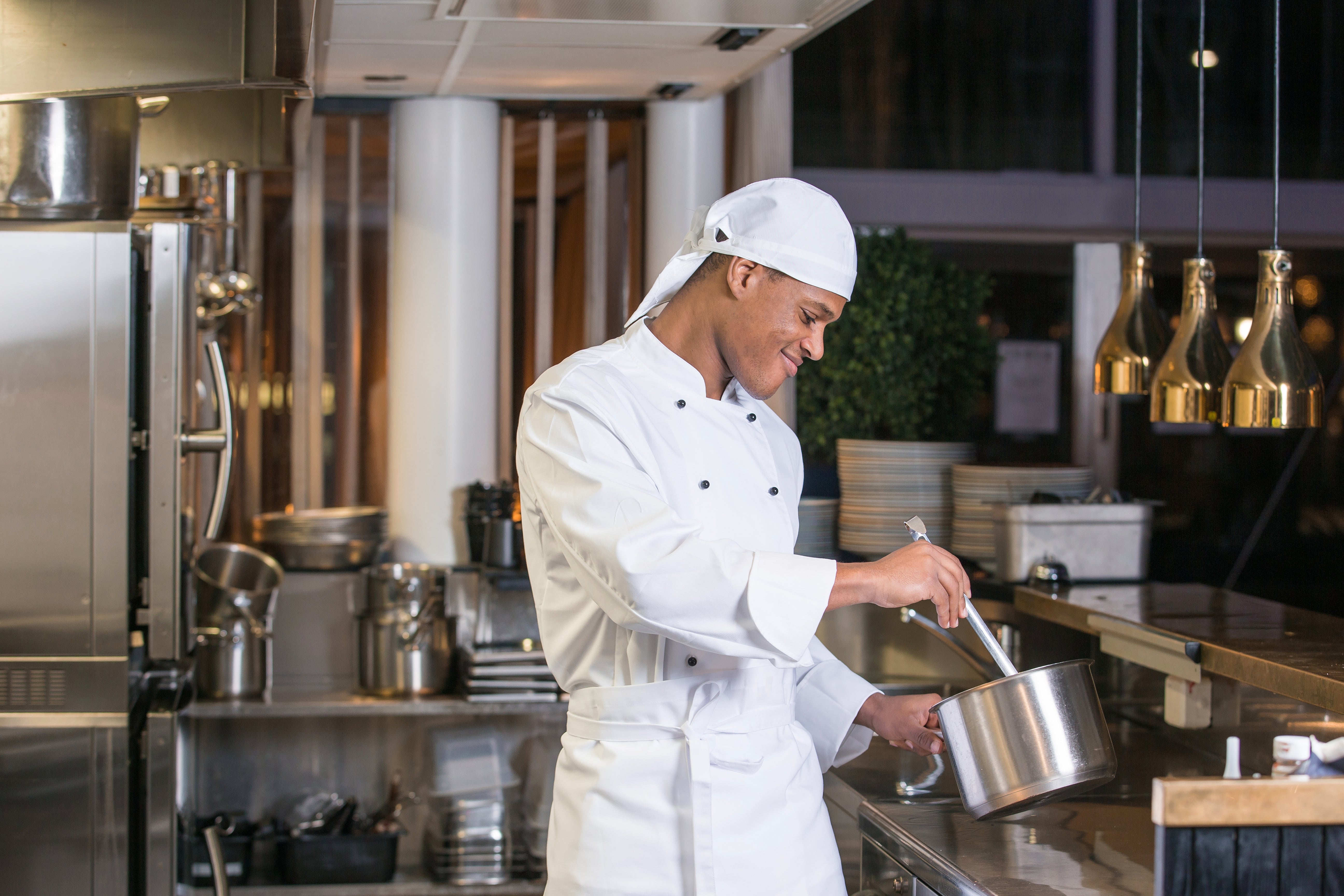 Kuvassa kokilla päässä Image Wearin valkoinen huivipäähine, kokin takki mustilla irtonapeilla sekä kokin esiliina. 