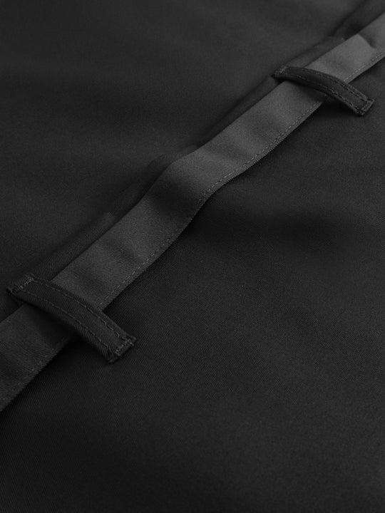 Yksityiskohtakuva mustan pitkän esiliinan vyötärönauhasta. 