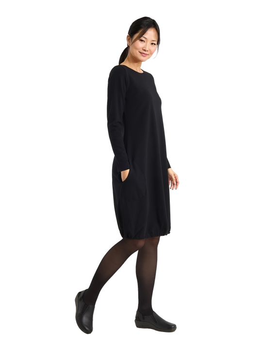 Kuvassa naismallilla päällä Image Wearin musta pitkähihainen ja taskullinen neulosmekko, jossa helmassa kiristysnauha. Jalassa mallilla on Image Wearin Rumba-nimiset työkengät.