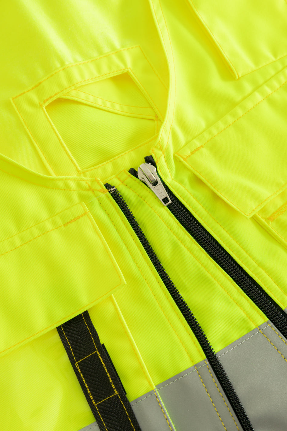 Yksityiskohtakuva keltaisen varoitusriipputaskuliivin etuvetoketjusta. 