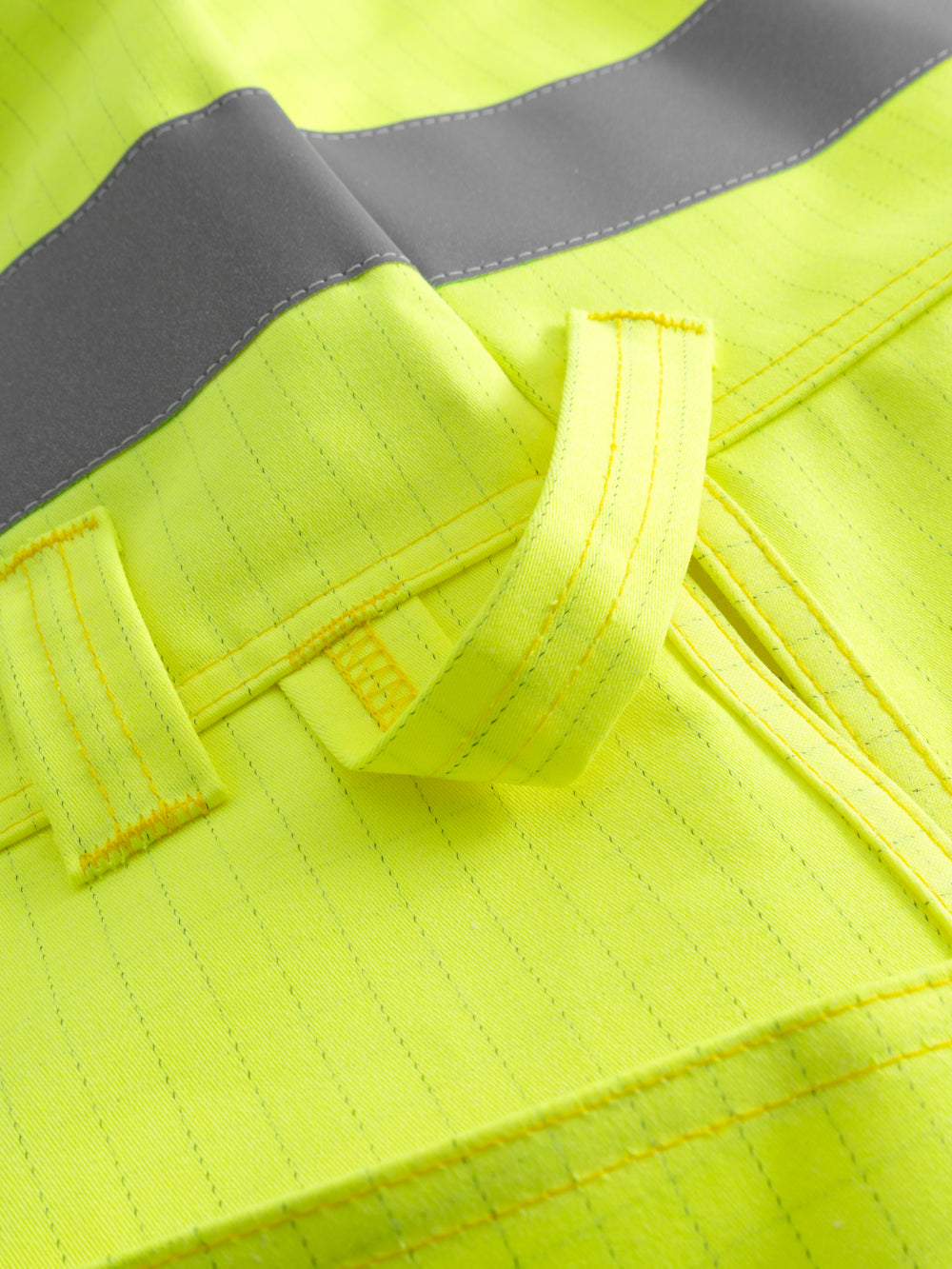 Yksityiskohtakuva keltaisen palosuojatun riipputaskuliivin heijastinnauhasta ja työkalulenkistä. 