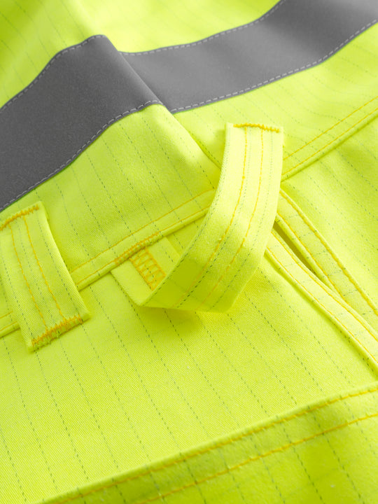 Yksityiskohtakuva keltaisen palosuojatun riipputaskuliivin heijastinnauhasta ja työkalulenkistä. 