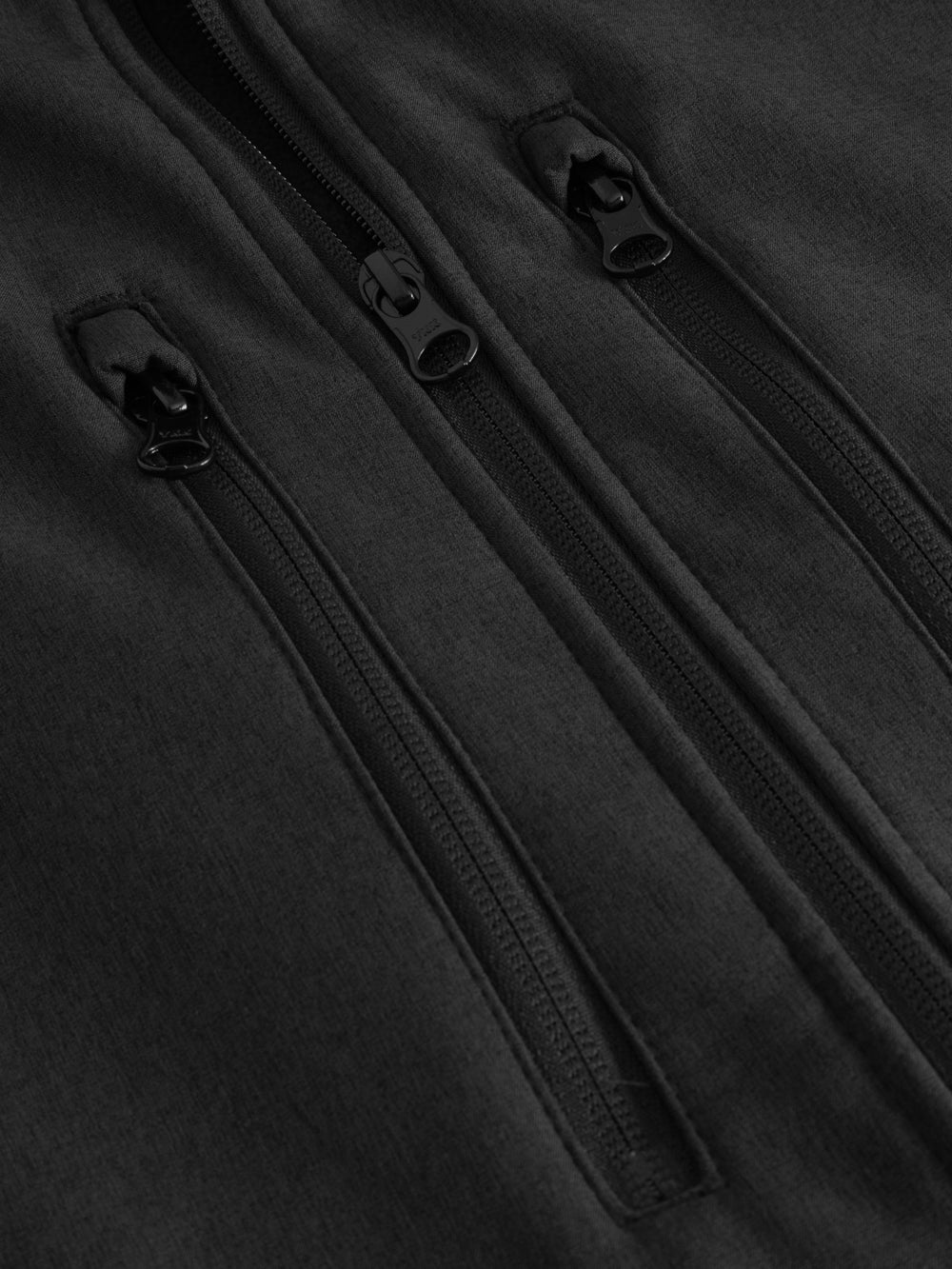 Yksityiskohtakuva meleeratun mustan softshell-liivin vetoketjuista. 