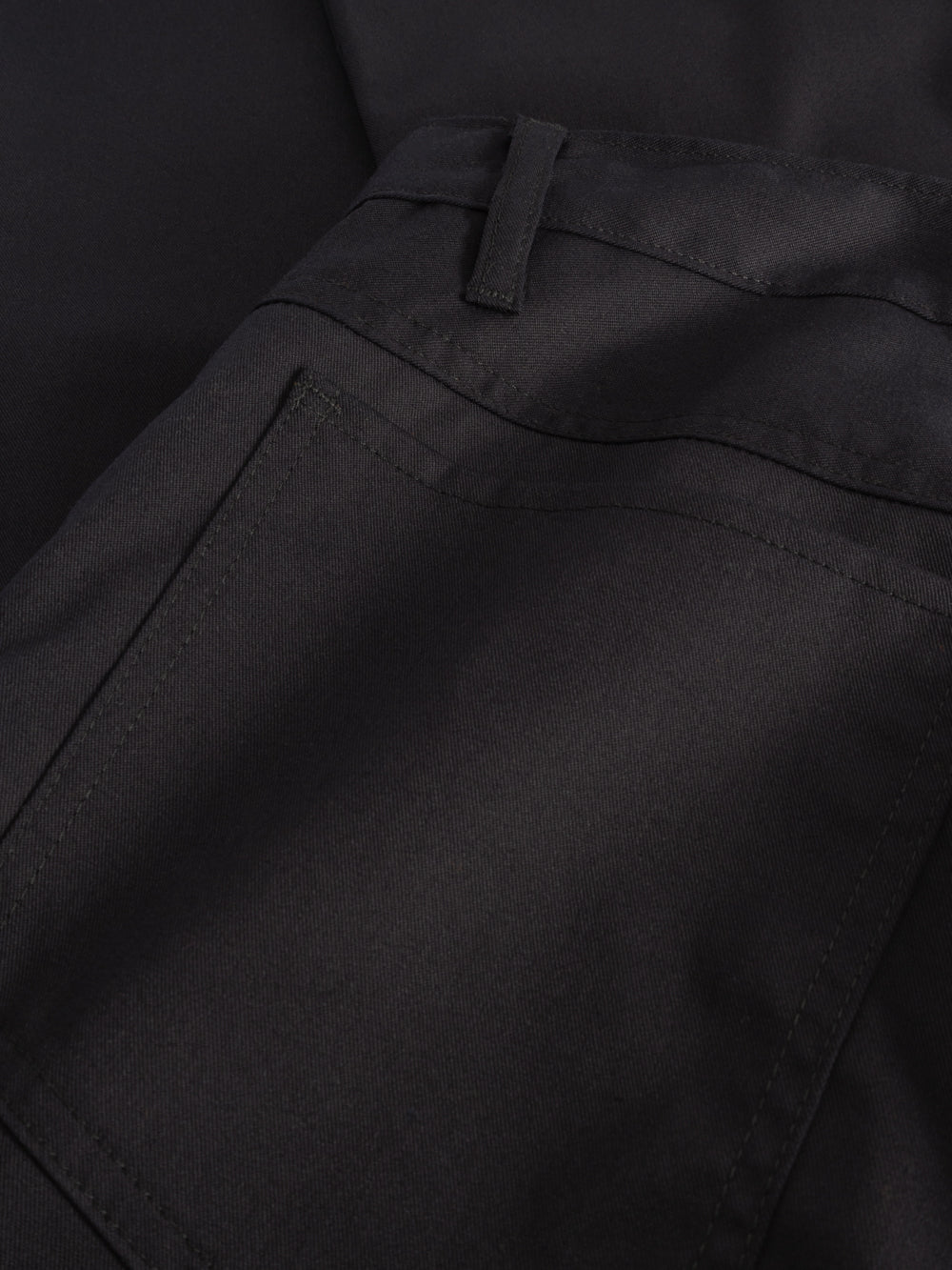 Yksityiskohtakuva tummansinisten farkkumallisten työhousujen takataskusta.