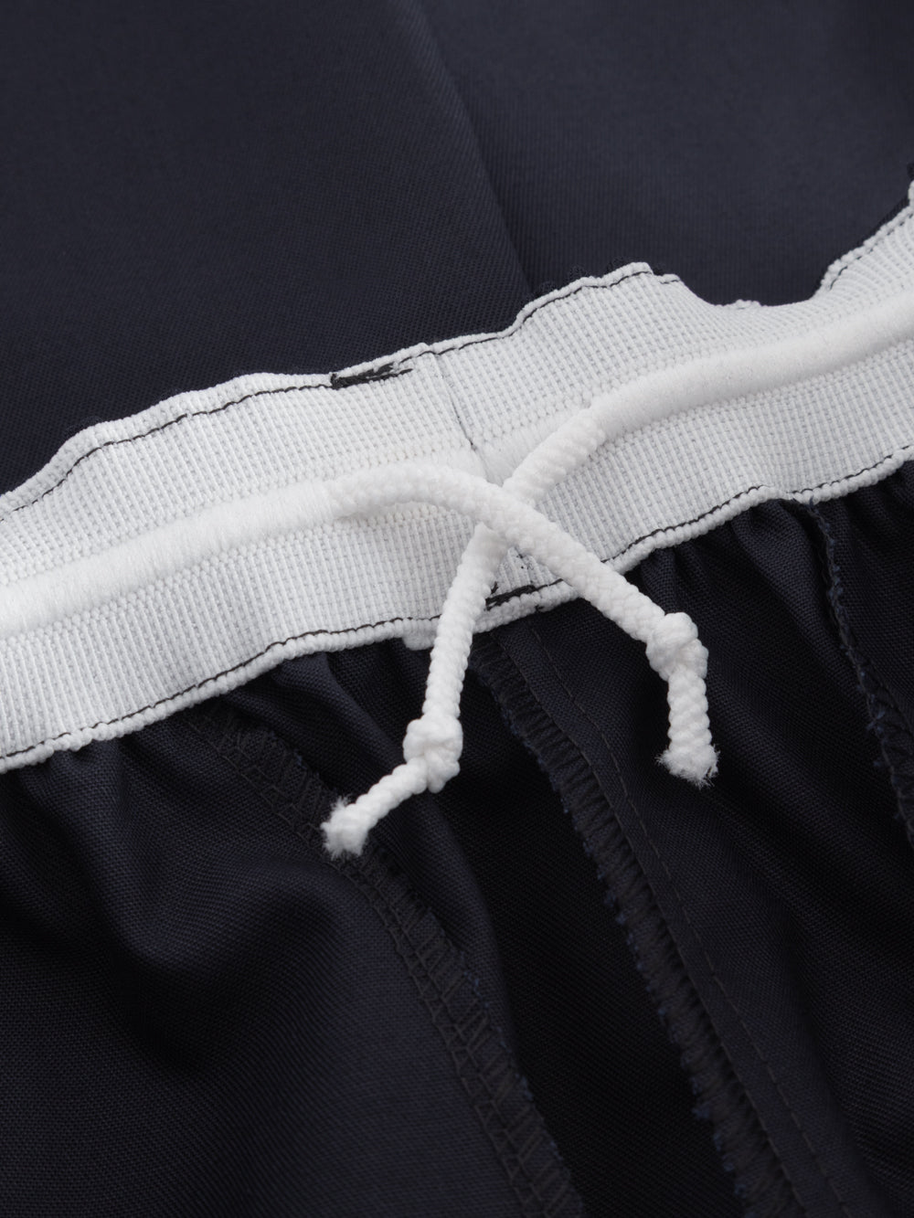 Yksityiskohtakuva tummansinisten housujen vyötäröllä olevasta kiristysnauhasta. 