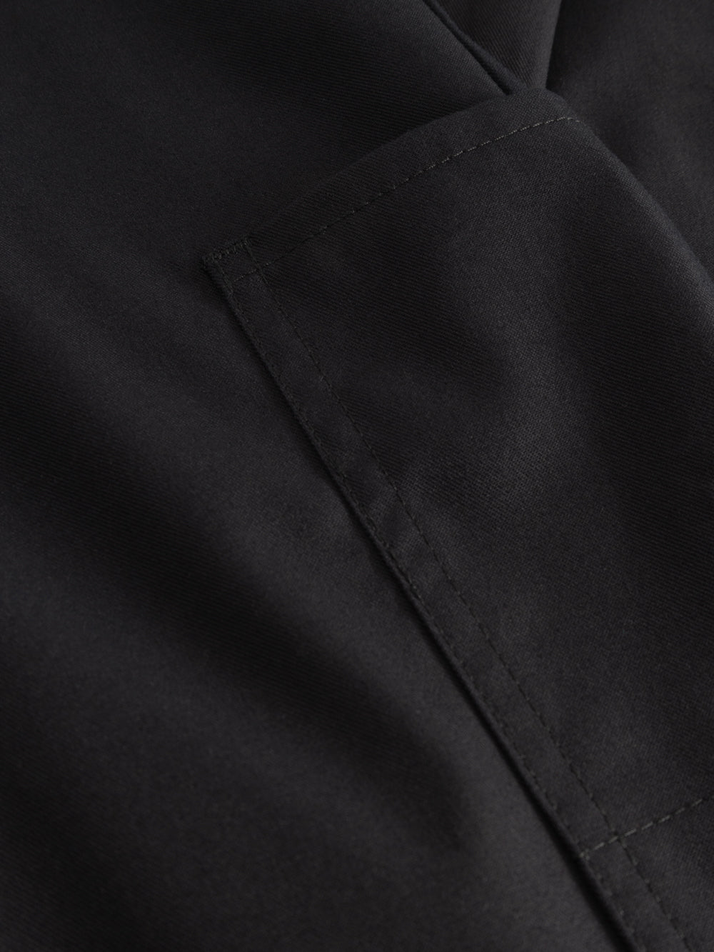 Yksityiskohtakuva tummansinisten mustien reisitaskuhousujen taskusta. 