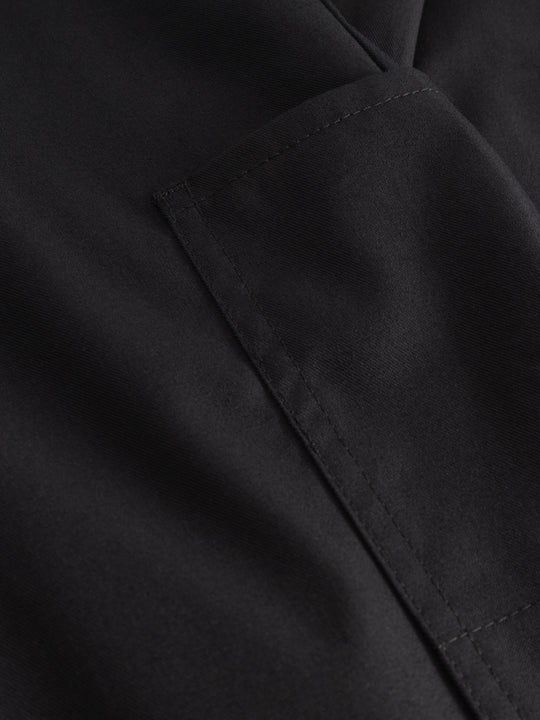 Yksityiskohtakuva tummansinisten mustien reisitaskuhousujen taskusta. 