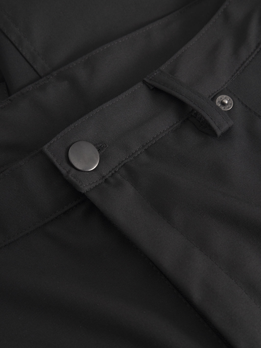 Miesten mustien reisitaskuhousujen vyötäröltä edestä tarkempi yksityiskohtakuva. 