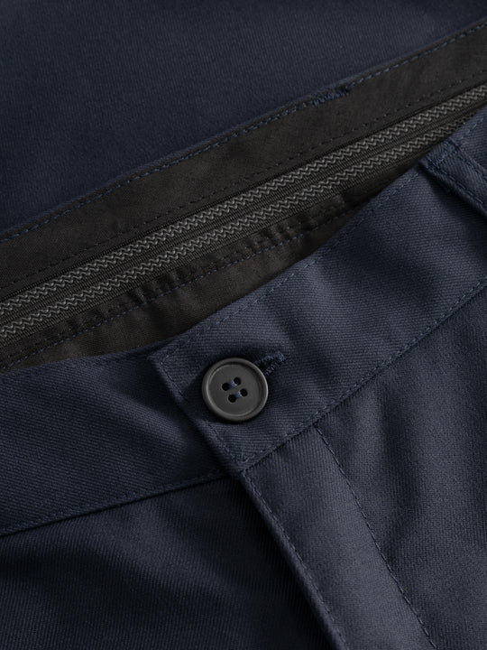 Yksityiskohtakuva tummansinisten housujen vyötärön nappikiinnityksestä ja vyötärökaitaleen sisäosasta. 