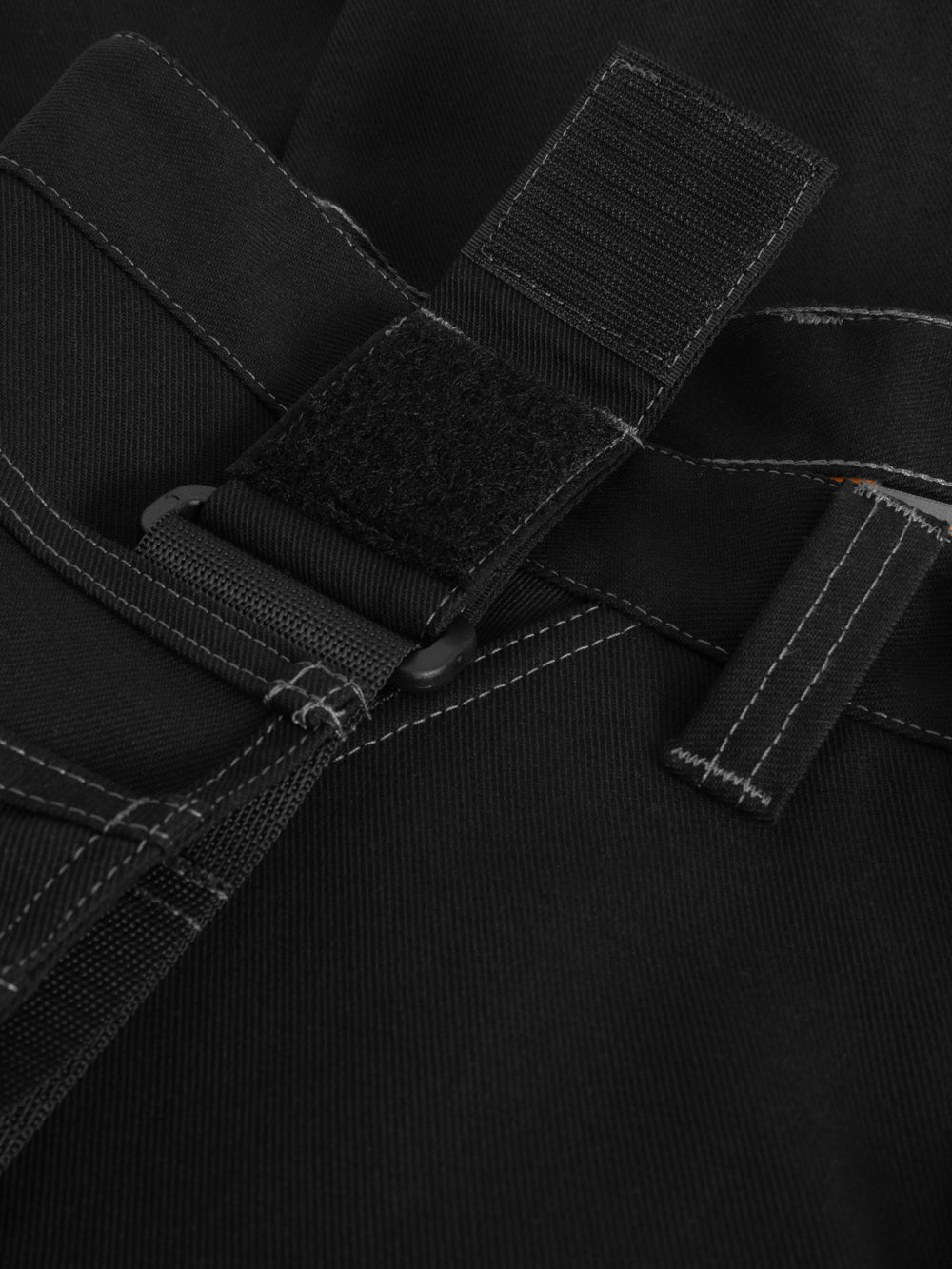 Yksityiskohtakuva mustien työhousujen riipputaskun kiinnityksestä. 