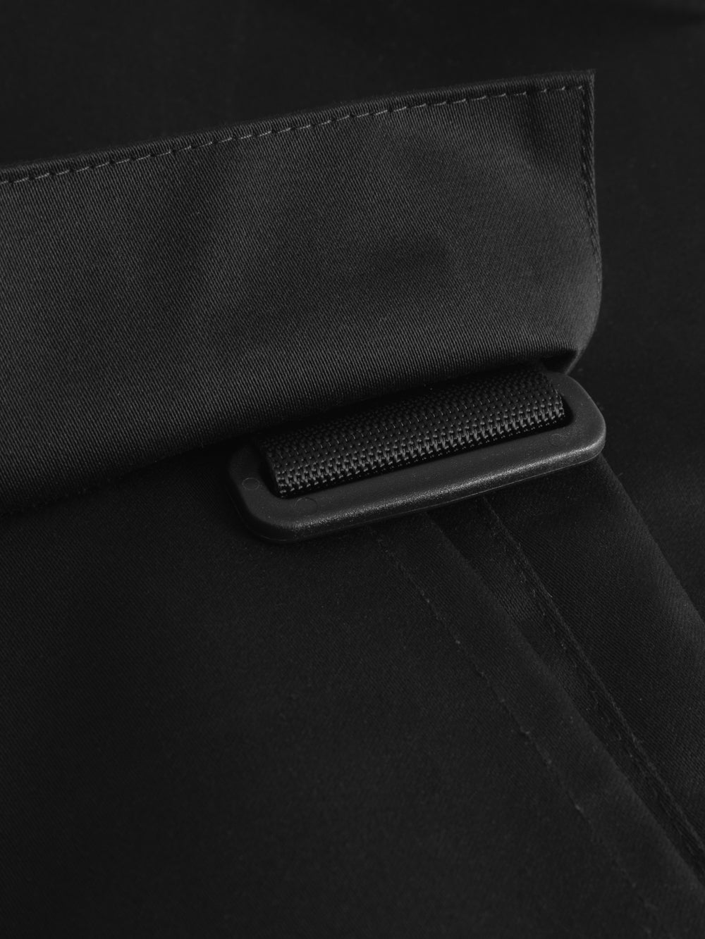 Yksityiskohtakuva palosuojattujen mustien työhousujen riipputaskujen kiinnityslenkistä. 