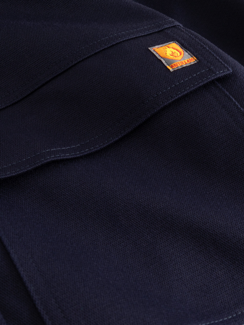 Yksityiskohtakuva tummansinisen palosuojatun työhaalarin taskusta ja antiflame-merkistä. 