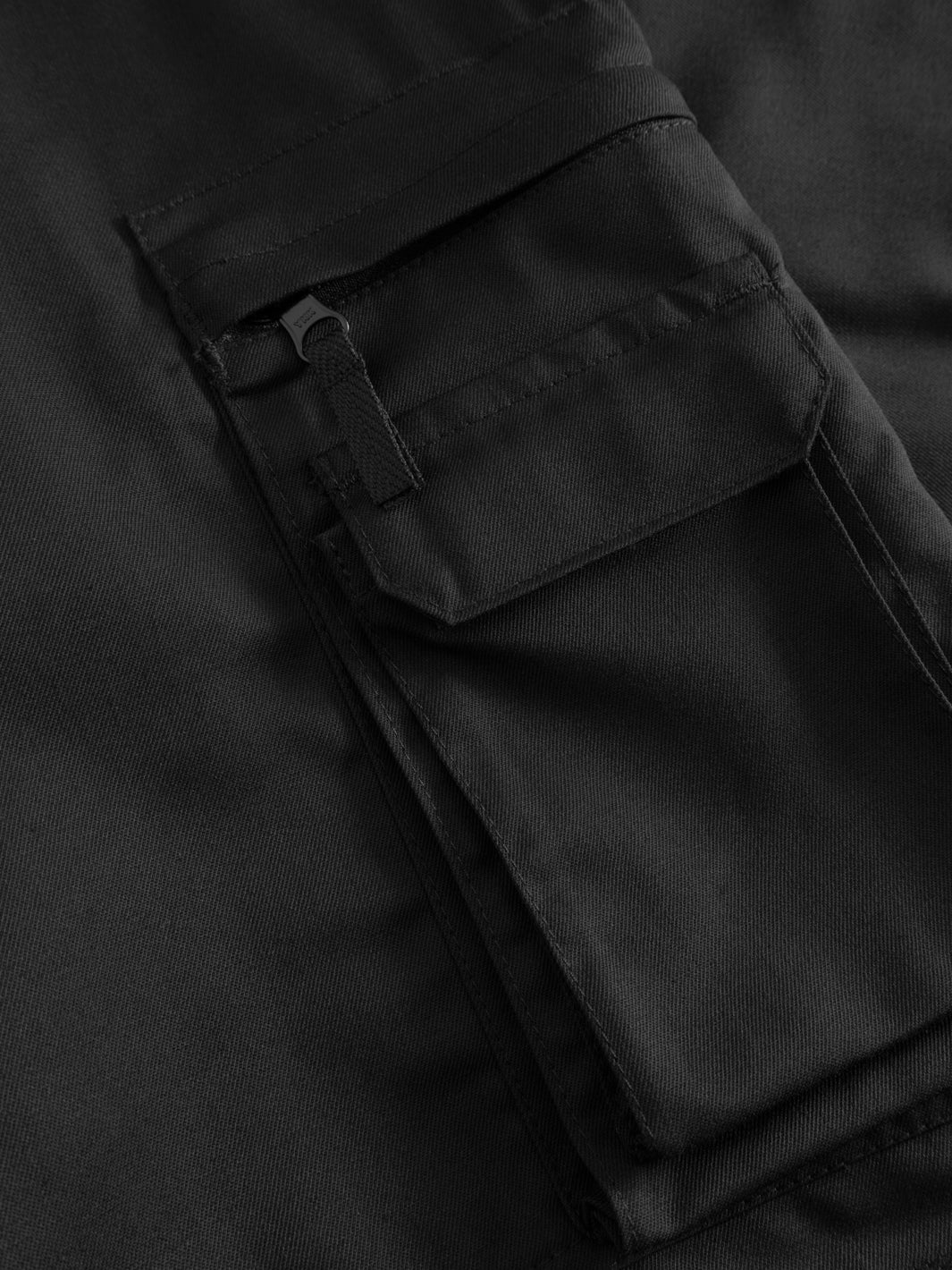 Yksityiskohtakuva mustan vartijahaalarin vetoketjullisesta reisitaskusta. 