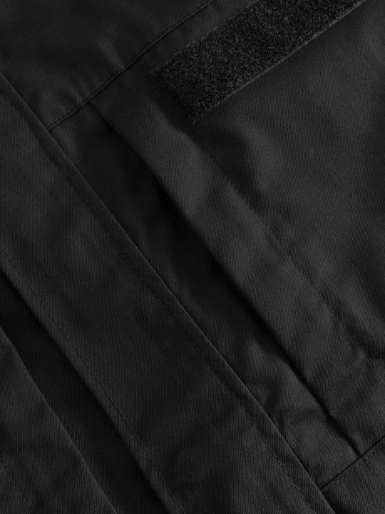 Yksityiskohtakuva mustan vartijahaalarin vetoketjullisesta rintataskusta ja tarrapaikasta virve-puhelimelle. 