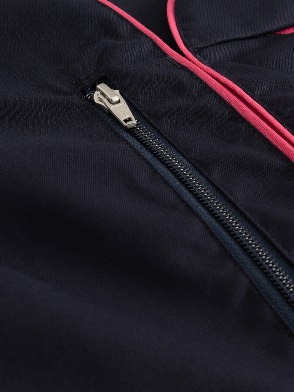 Yksityiskohtakuva tummansinisen tunikan rintataskun vetoketjusta. 