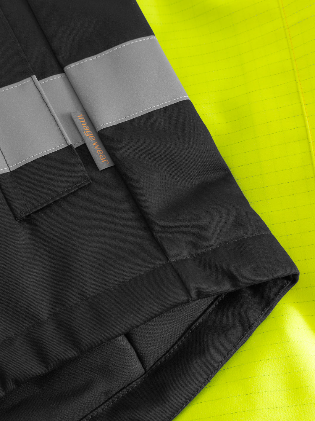 Yksityiskohtakuva keltaisen näkyvän palosuojatun takin helmasta ja sivussa olevasta Image Wearin tuotemerkistä.