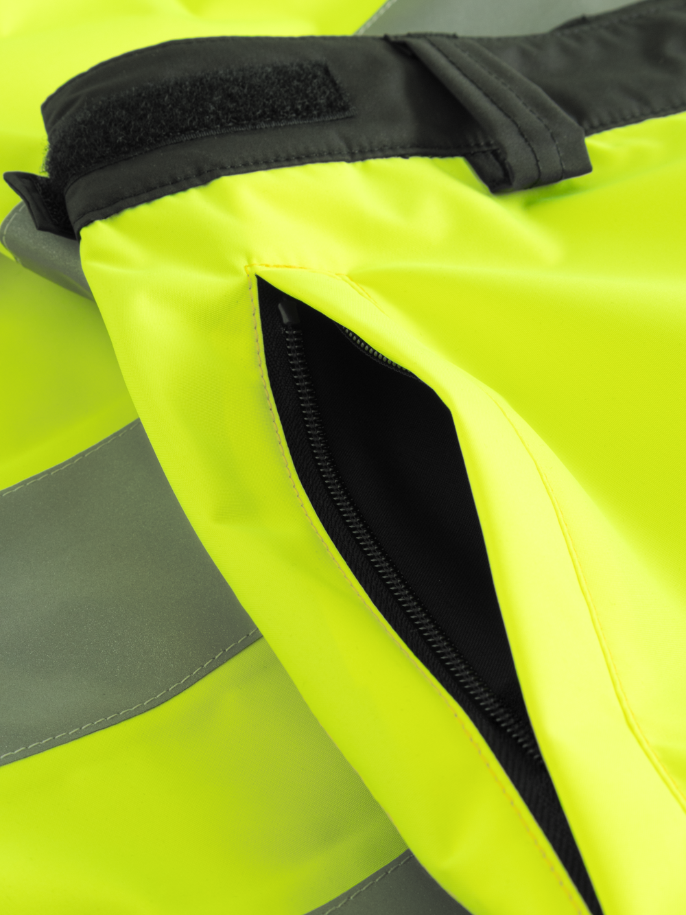 Yksityiskohtakuva keltaisten varoituskuorihousujen vetoketjullisesta sivutaskusta. 