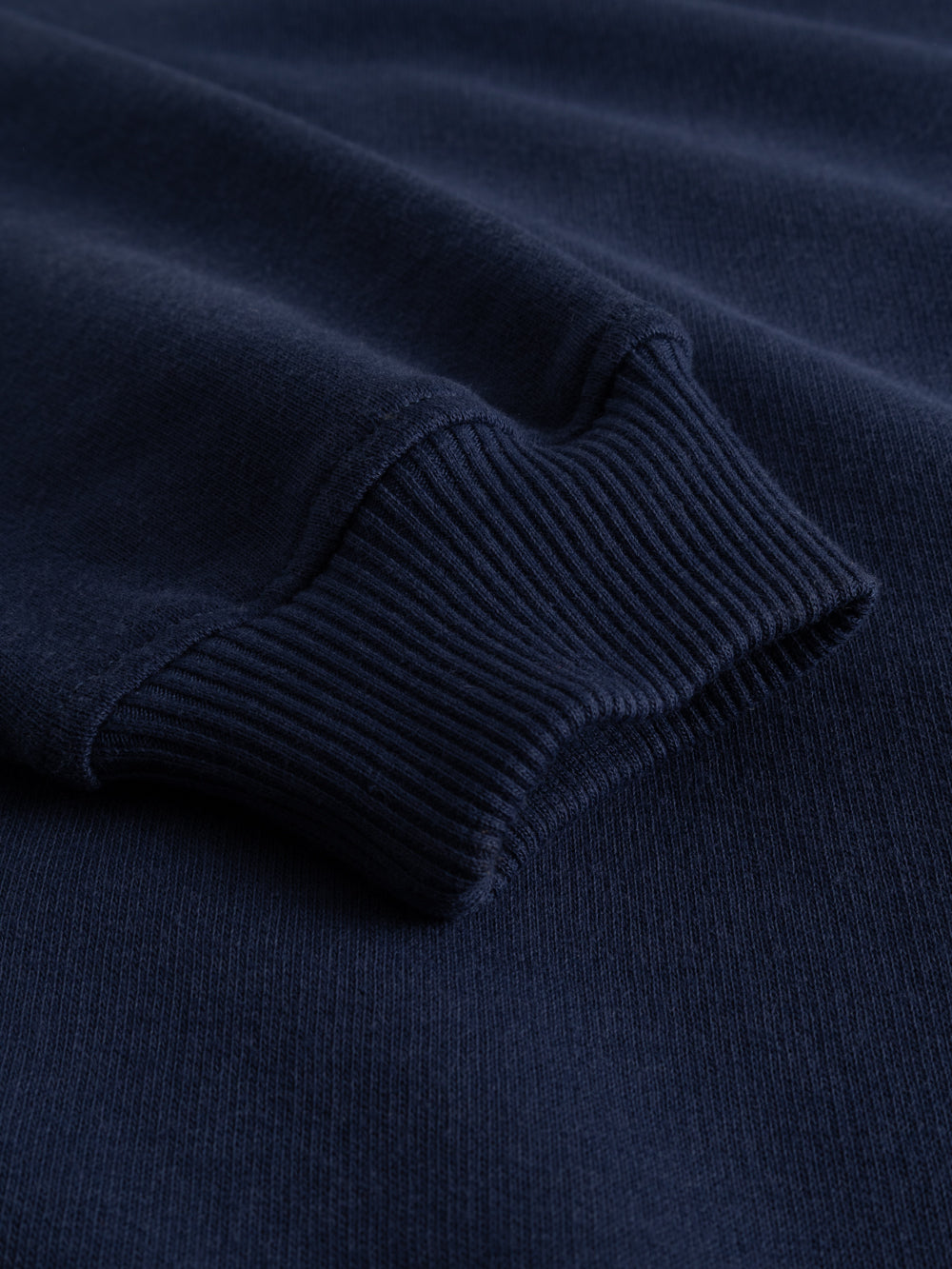 Yksityiskohtakuva tummansinisen collegepaidan hihansuusta. 