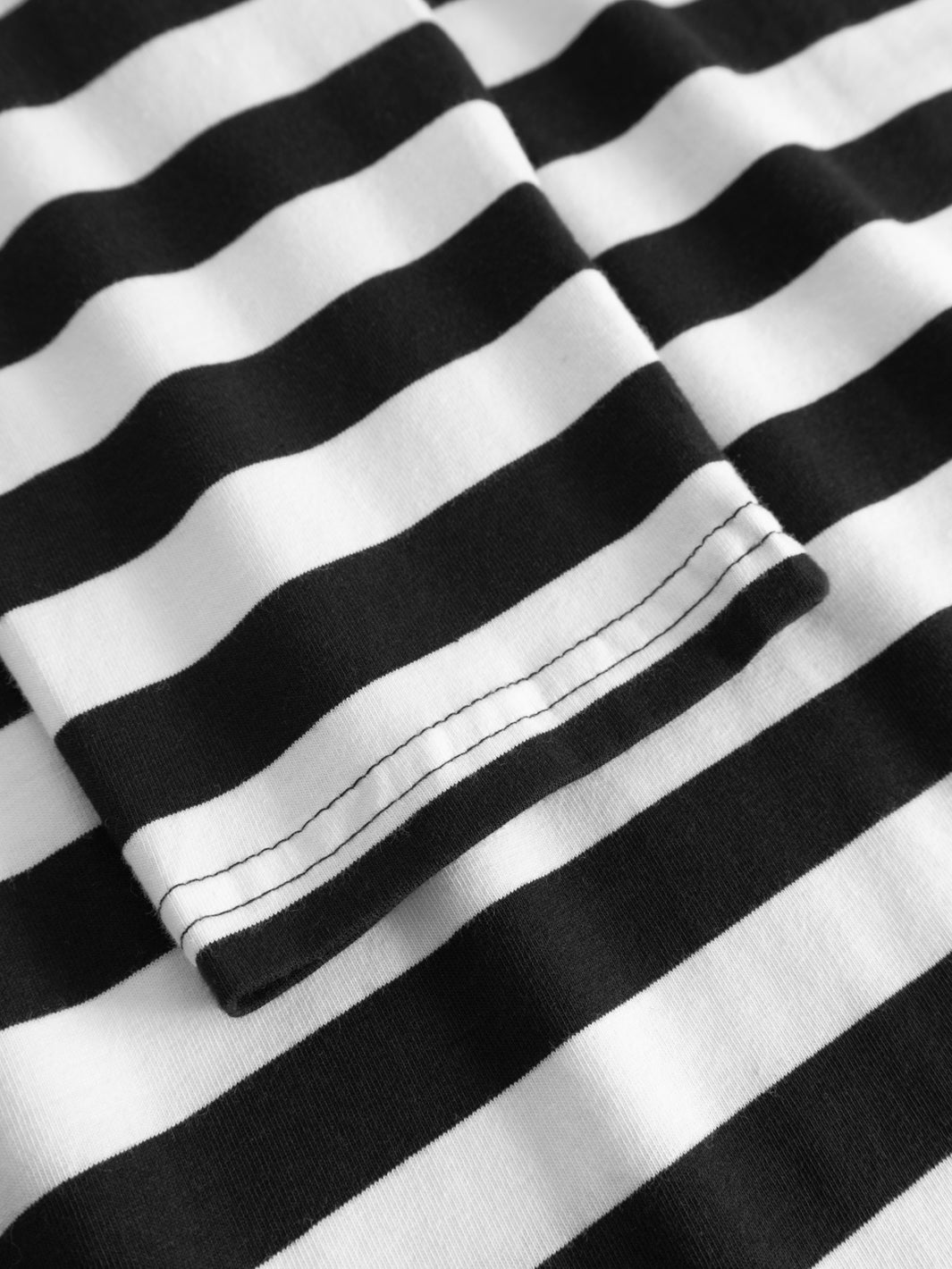 Yksityiskohtakuva mustavalkoraidallisen trikoopaidan hihansuusta. 