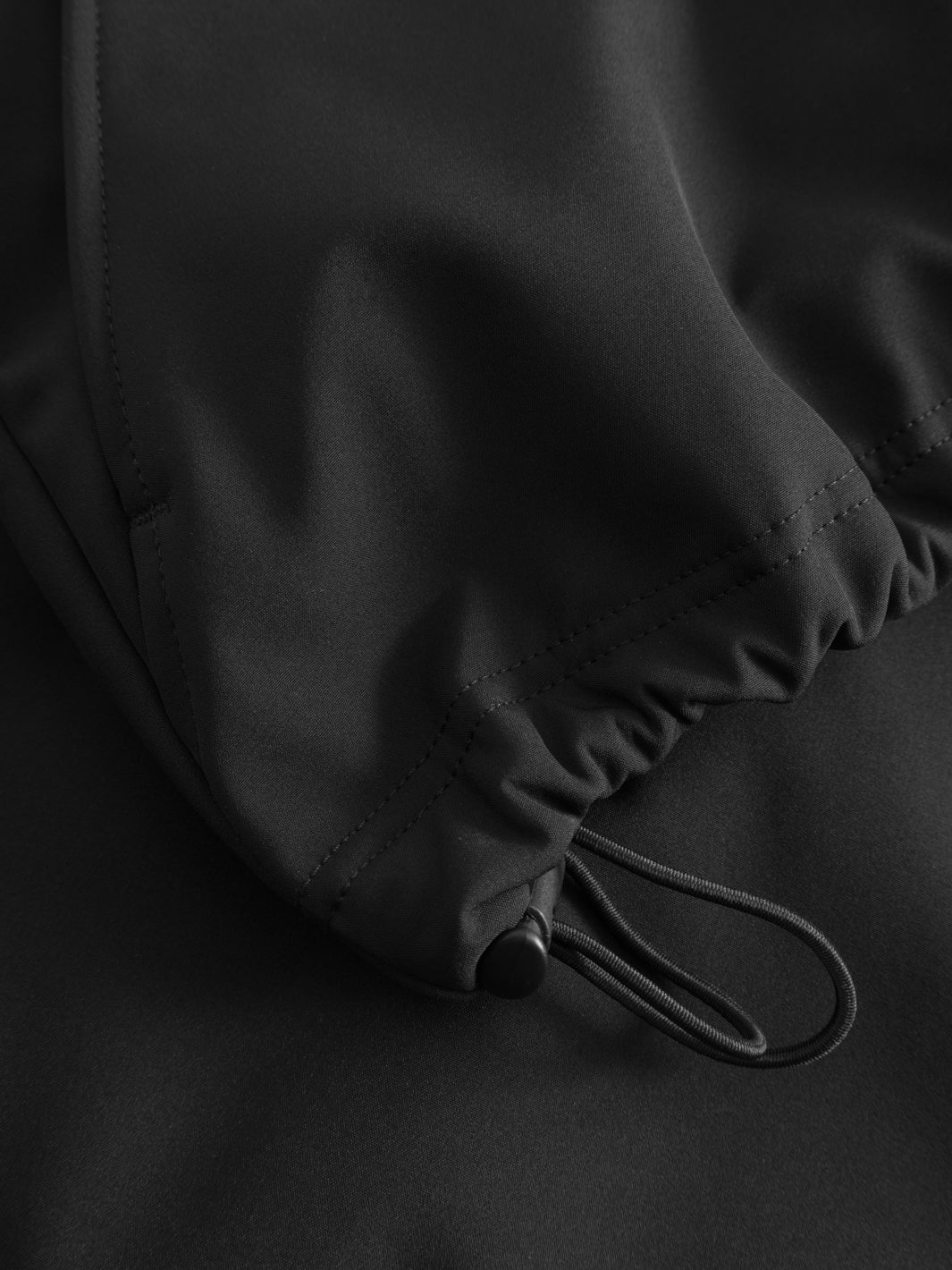 Yksityiskohtakuva mustan välikausitakin helman kiristysnauhasta.