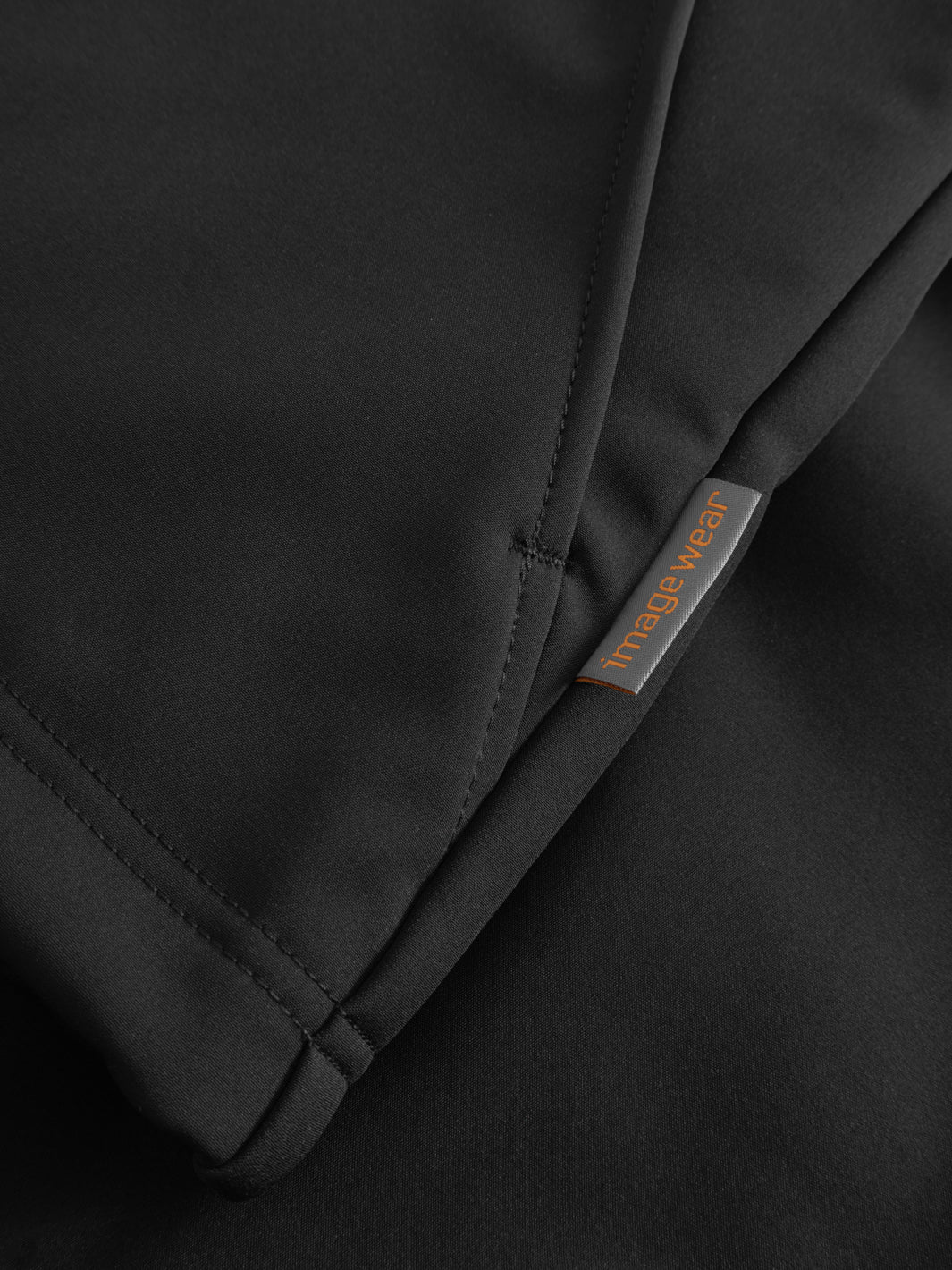 Yksityiskohtakuva mustan välikausitakin sivusaumasta ja Image Wearin merkistä. 