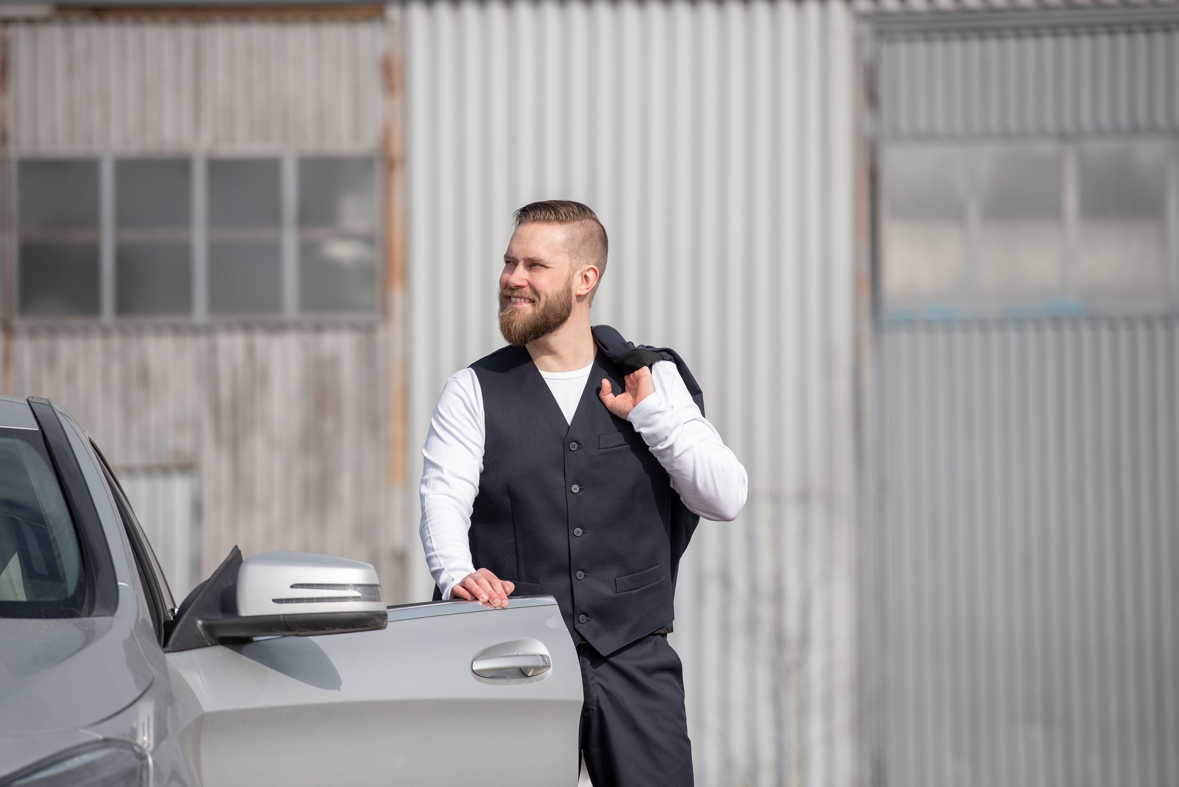 Kuvassa miehellä musta liivi ja suorat housut sekä valkoinen trikoopaita ja olalla musta puvun takki Image Wearin mallistosta.