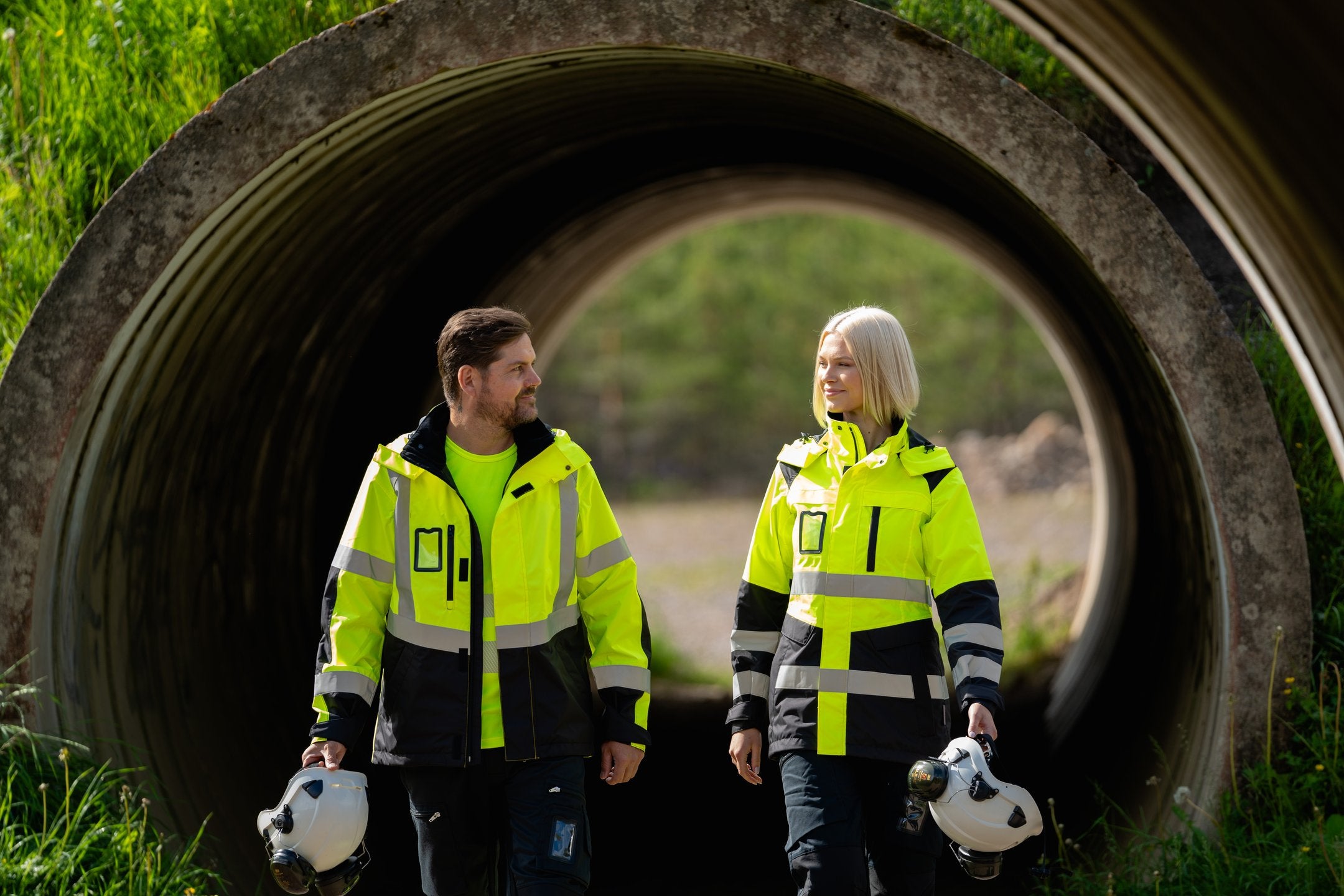 Kuvassa nainen ja mies keltaisissa Image Wearin varoituskuoritakeissa. Kädessä molemmilla on Petzlin valkoinen turvakypärä.