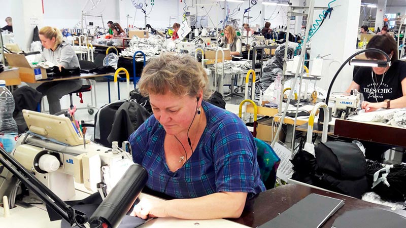 Image Wear Narvan tehtaan työntekijä työssään ompelukoneen äärellä. Samassa salissa työskentelee useampi ompelija.